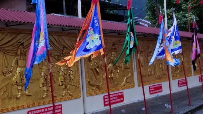Gambar Kwan Kong berwarna emas di dinding yang disertai dengan beragam bendera