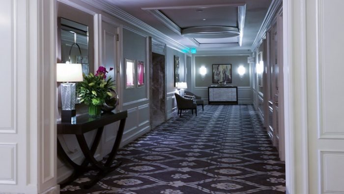 Koridor ke kamar hotel dengan karpet mewah dan meja pajangan bunga