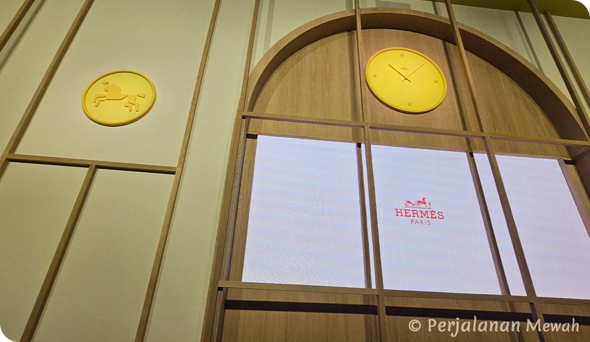 Hermès welcome room with bright yellow wall clock and symbolic horse plaque above illuminated logo screen