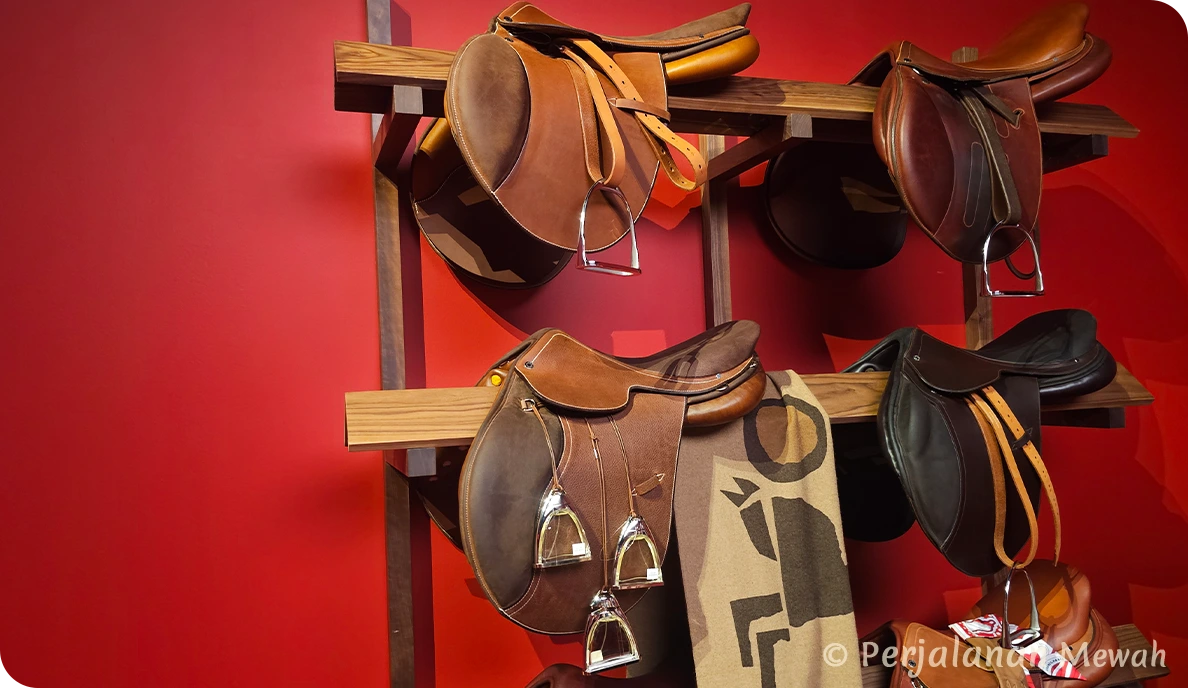 Hermès leather saddles on display against bold red wall in the Head Groom’s Office